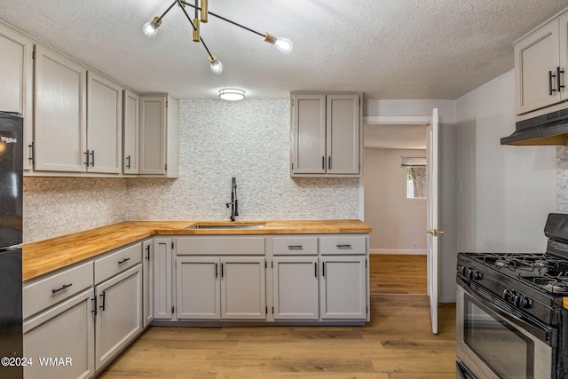 kitchen with stainless steel gas range oven, butcher block counters, light wood-style flooring, under cabinet range hood, and a sink