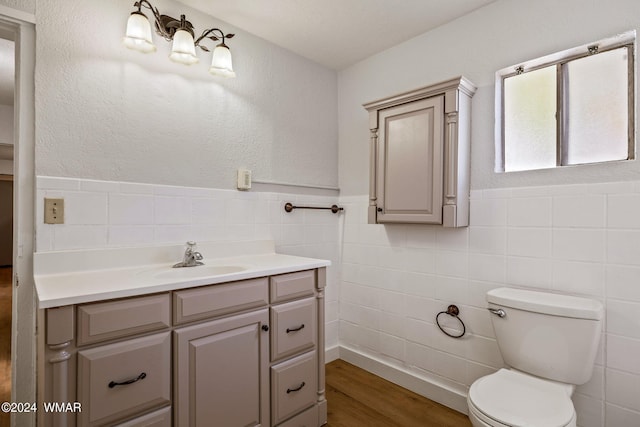 bathroom featuring tile walls, toilet, wainscoting, vanity, and wood finished floors