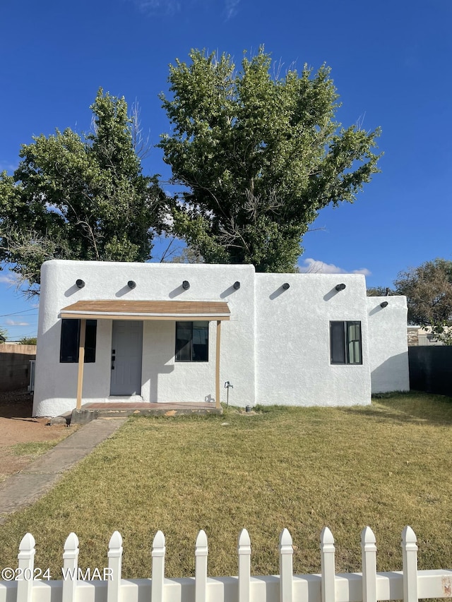 pueblo-style home with a front yard, fence, and stucco siding