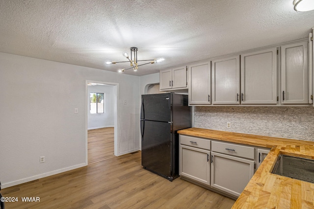 kitchen with light wood-type flooring, wood counters, a notable chandelier, and freestanding refrigerator