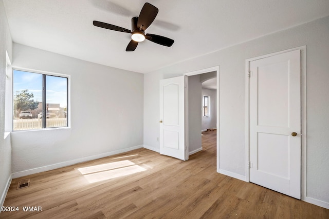 unfurnished bedroom featuring arched walkways, visible vents, ceiling fan, light wood-type flooring, and baseboards