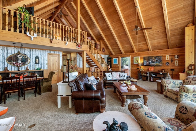 carpeted living room featuring beam ceiling, a ceiling fan, wood ceiling, wood walls, and stairs