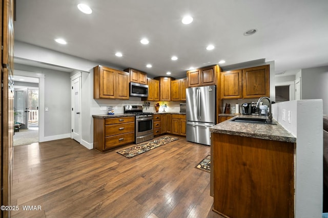 kitchen featuring brown cabinets, dark wood finished floors, stainless steel appliances, recessed lighting, and a sink