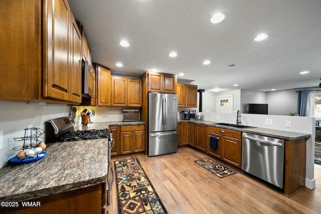 kitchen with stainless steel appliances, brown cabinetry, a sink, light wood-type flooring, and a peninsula