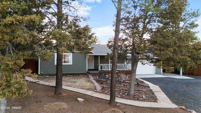 ranch-style home featuring an attached garage, covered porch, a shingled roof, fence, and driveway