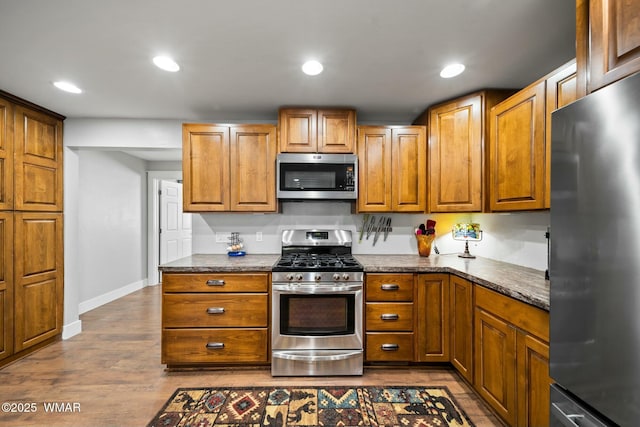 kitchen with appliances with stainless steel finishes, recessed lighting, brown cabinetry, and dark wood-type flooring