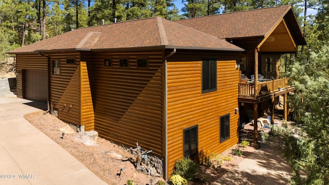 view of side of home featuring a shingled roof, faux log siding, and a detached garage