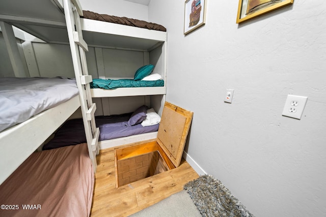 bedroom featuring baseboards, a textured wall, and wood finished floors