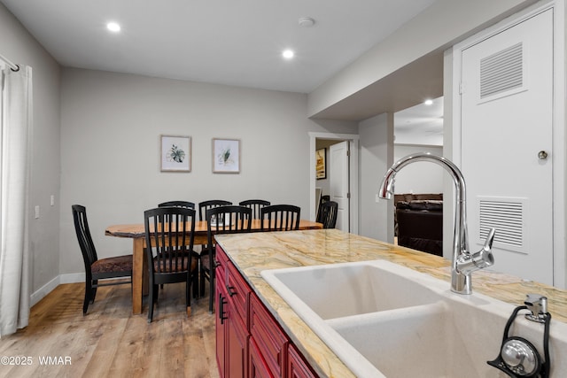 kitchen with a sink, light wood finished floors, recessed lighting, reddish brown cabinets, and visible vents