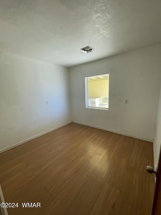 empty room with visible vents, a textured ceiling, baseboards, and wood finished floors