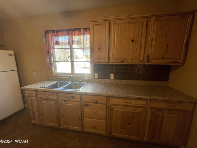 kitchen with brown cabinetry, freestanding refrigerator, a sink, and decorative backsplash