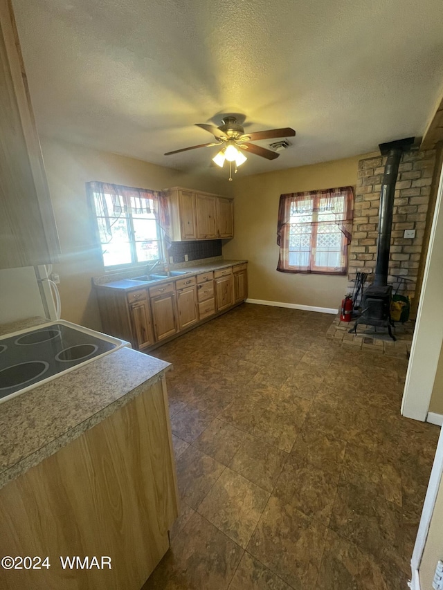 kitchen with a ceiling fan, a wood stove, light countertops, a textured ceiling, and a sink