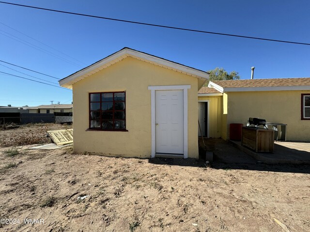 rear view of house with a shingled roof, fence, and stucco siding