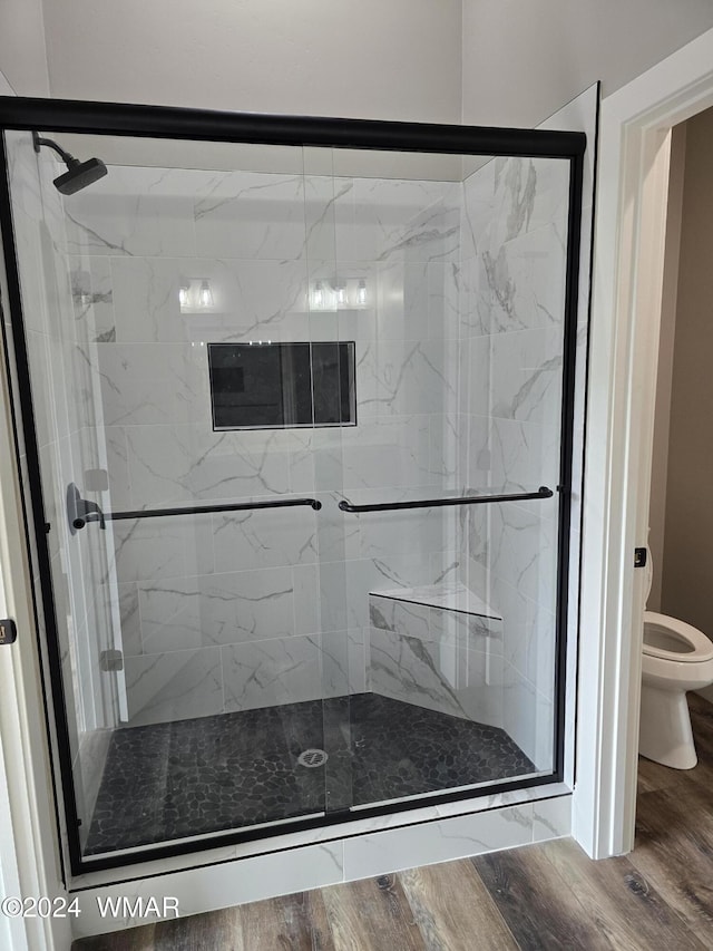 bathroom with a stall shower, toilet, and wood finished floors