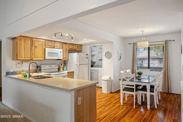 kitchen featuring white appliances, wood finished floors, a peninsula, light countertops, and a sink