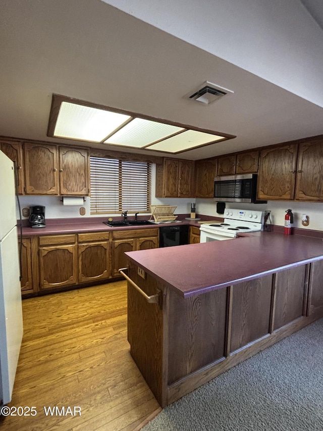 kitchen featuring visible vents, a sink, dark countertops, white appliances, and a peninsula