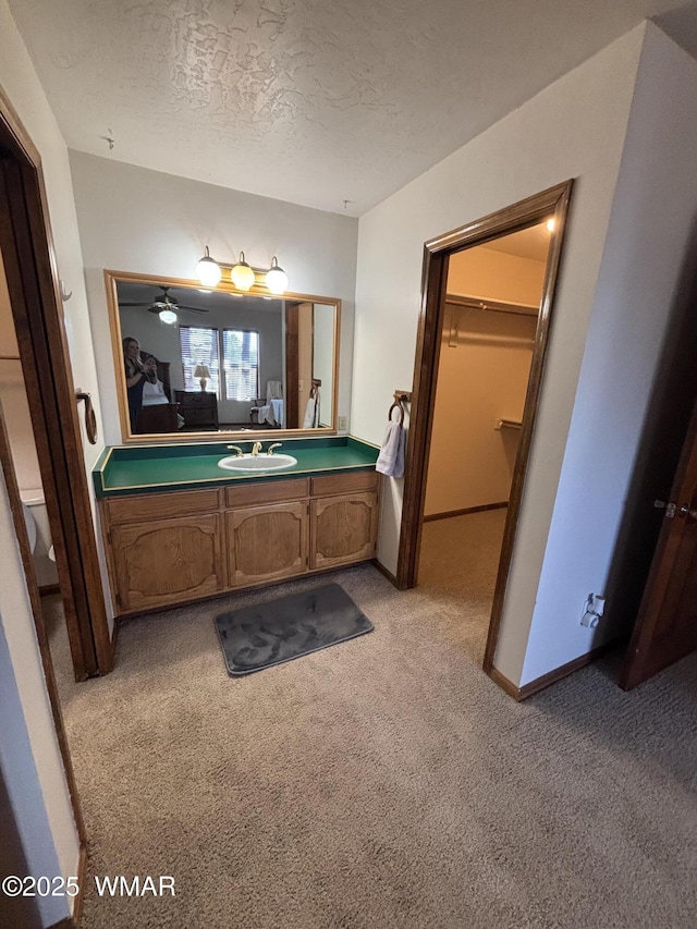 bathroom with a spacious closet, baseboards, vanity, carpet flooring, and a textured ceiling