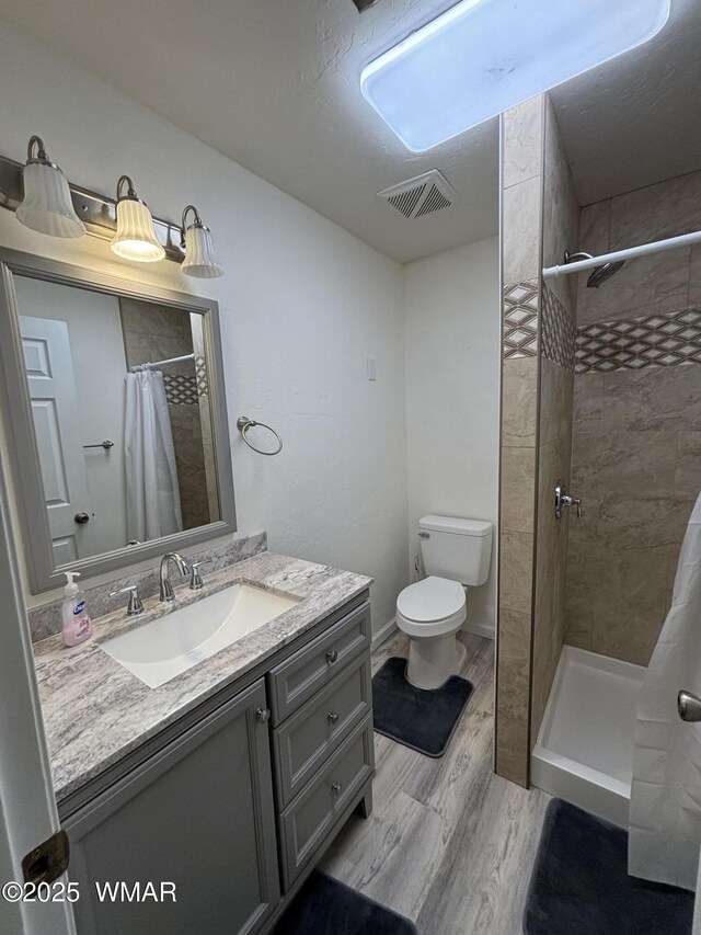 bathroom featuring vanity, wood finished floors, visible vents, a tile shower, and toilet