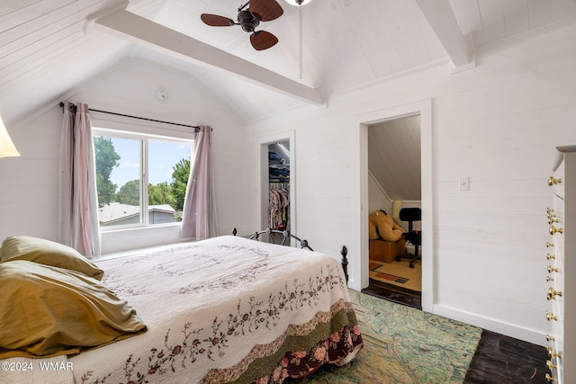 bedroom featuring dark wood finished floors, a ceiling fan, lofted ceiling with beams, a walk in closet, and wood walls