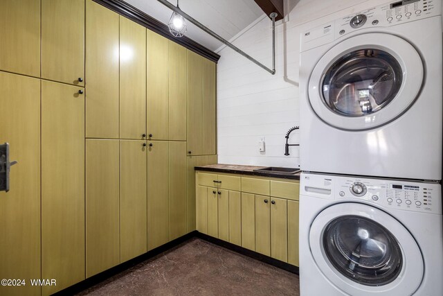 clothes washing area with a sink, cabinet space, and stacked washer / drying machine