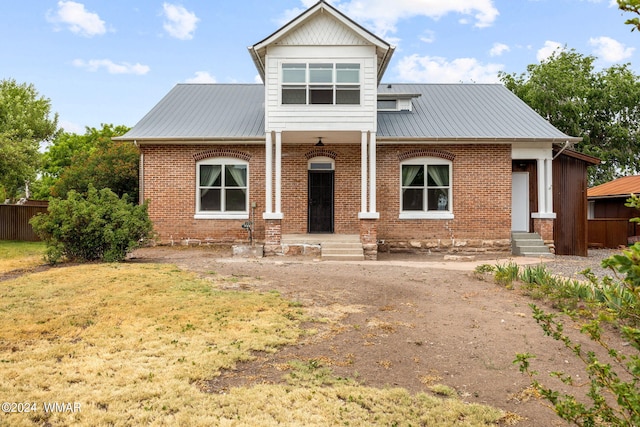 view of front of house with a front yard, brick siding, metal roof, and fence