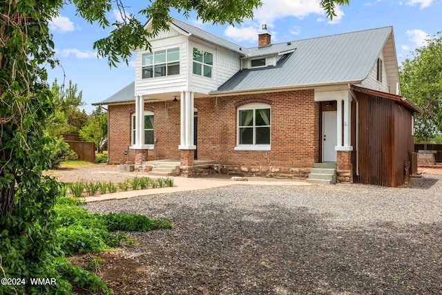 rear view of house with entry steps, brick siding, metal roof, and a chimney