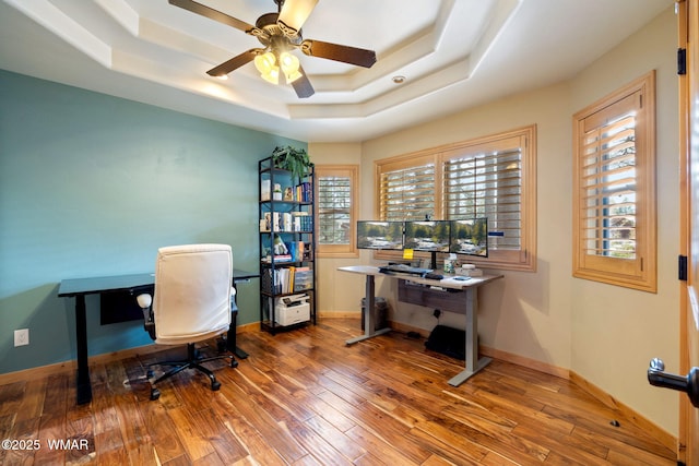 home office featuring a tray ceiling, wood finished floors, and baseboards