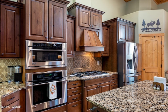 kitchen with backsplash, light stone countertops, custom exhaust hood, and appliances with stainless steel finishes