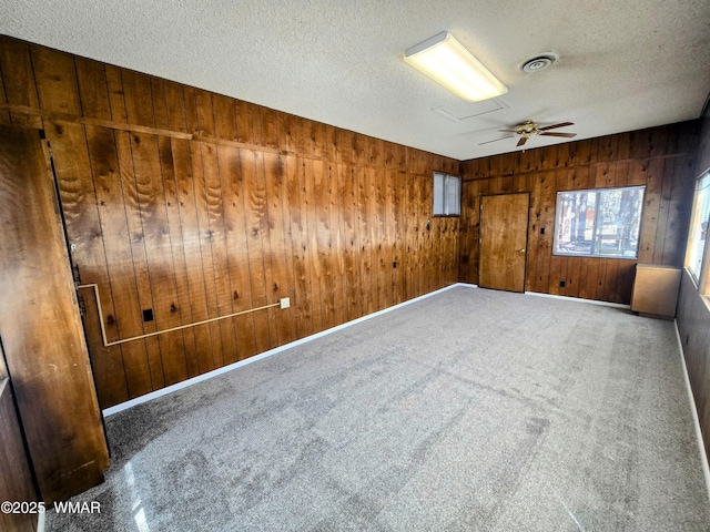 unfurnished room with a textured ceiling, wood walls, a wealth of natural light, visible vents, and ceiling fan