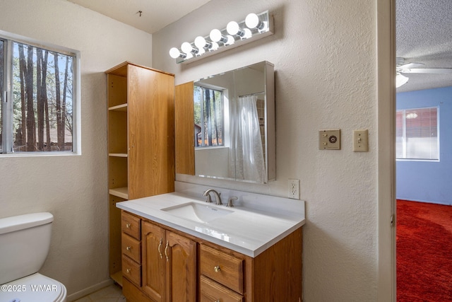 full bathroom with toilet, a textured wall, vanity, and a ceiling fan