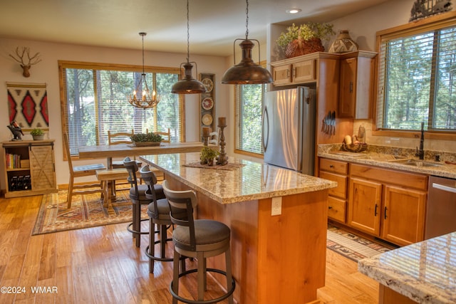 kitchen featuring light wood-style flooring, a kitchen island, hanging light fixtures, stainless steel appliances, and a sink