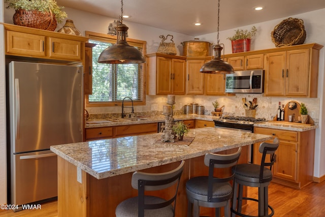 kitchen featuring a center island, decorative light fixtures, stainless steel appliances, light wood-style floors, and a sink