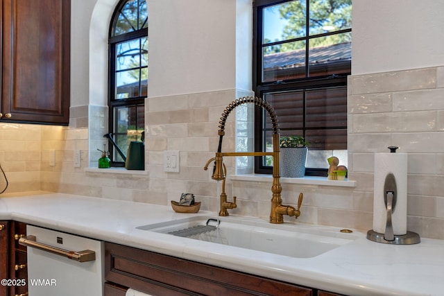 interior space with white dishwasher, a sink, dark brown cabinetry, and light stone countertops