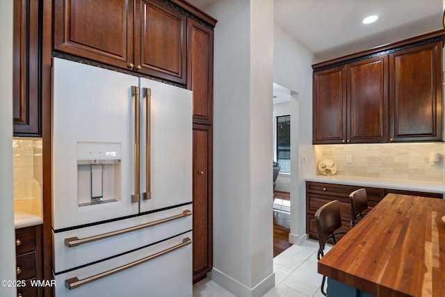 kitchen with baseboards, decorative backsplash, wood counters, high end white fridge, and dark brown cabinets