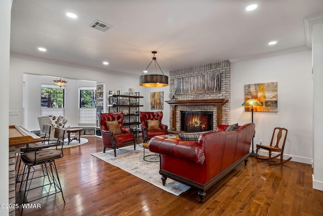 living area with visible vents, ornamental molding, a brick fireplace, baseboards, and hardwood / wood-style flooring