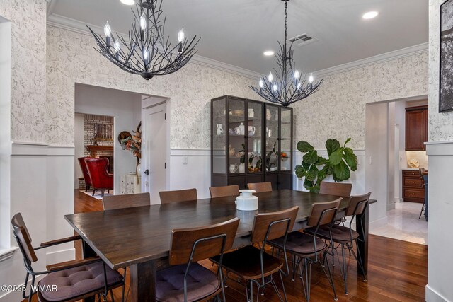 dining space with wallpapered walls, a wainscoted wall, ornamental molding, wood finished floors, and a chandelier