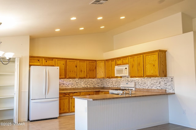 kitchen featuring a notable chandelier, tasteful backsplash, brown cabinetry, white appliances, and a peninsula