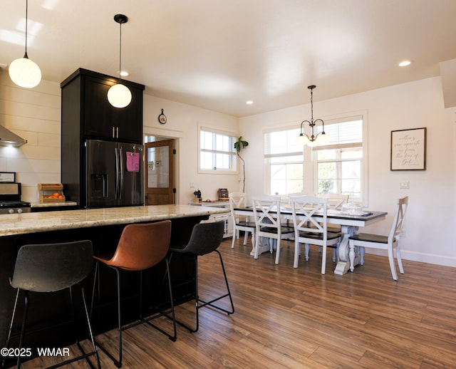 kitchen with dark wood finished floors, recessed lighting, fridge with ice dispenser, light stone countertops, and dark cabinetry