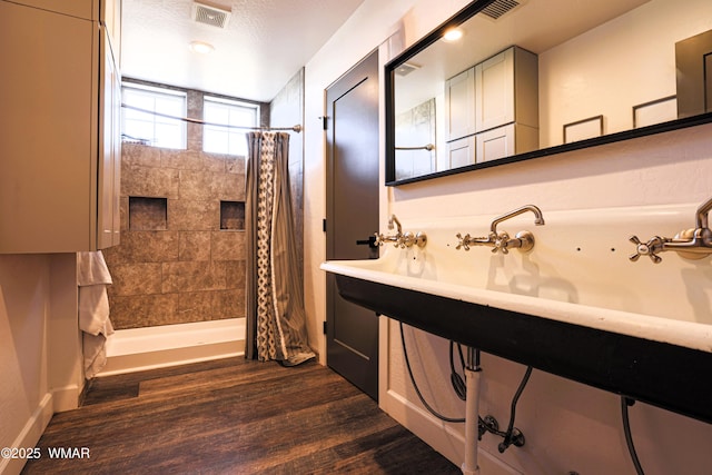 full bathroom featuring a tile shower, wood finished floors, and visible vents