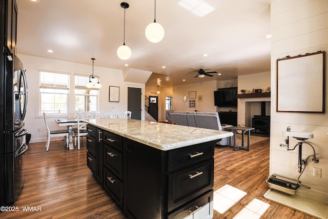 kitchen featuring a wood stove, dark wood-style flooring, dark cabinets, and freestanding refrigerator