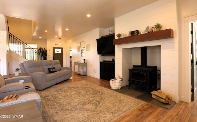 living room with recessed lighting, wood finished floors, baseboards, stairway, and a wood stove