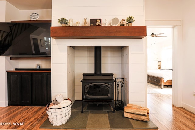 interior details with baseboards, wood finished floors, a wood stove, and a ceiling fan