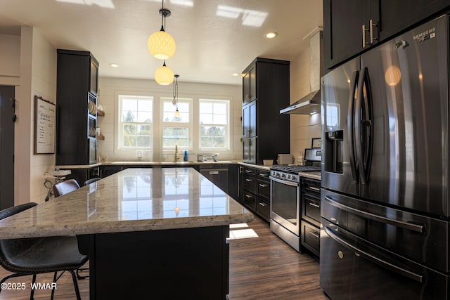 kitchen with a center island, a breakfast bar area, stainless steel appliances, dark cabinets, and wall chimney exhaust hood