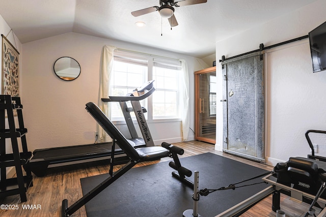 workout area with lofted ceiling, ceiling fan, a barn door, wood finished floors, and baseboards