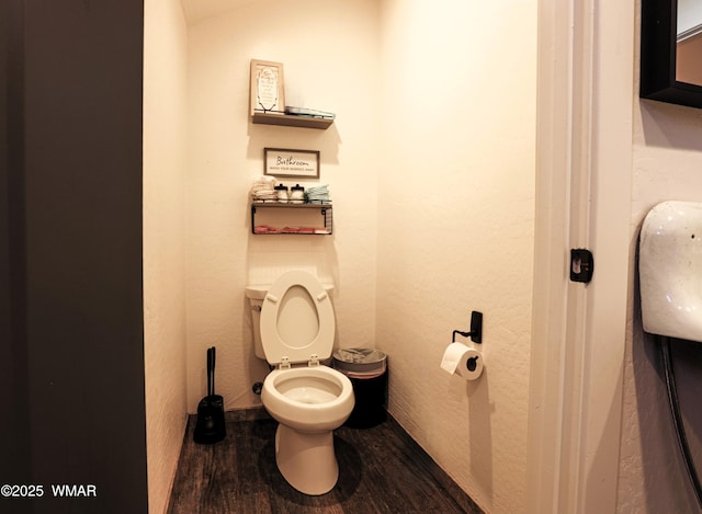 bathroom with a textured wall, toilet, and wood finished floors