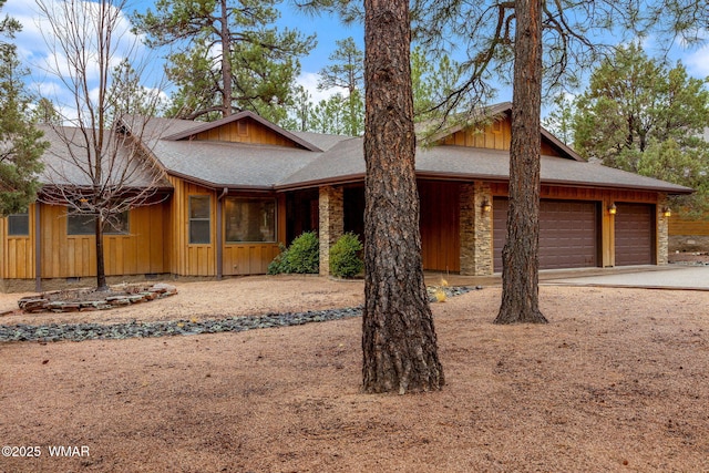 chalet / cabin featuring driveway, a shingled roof, stone siding, an attached garage, and board and batten siding