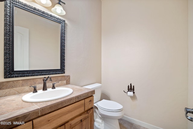 half bath with baseboards, vanity, and toilet