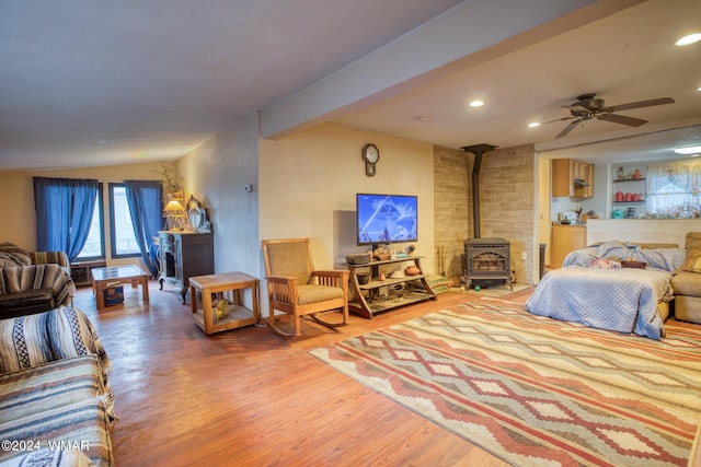 bedroom with recessed lighting, a wood stove, beam ceiling, and wood finished floors