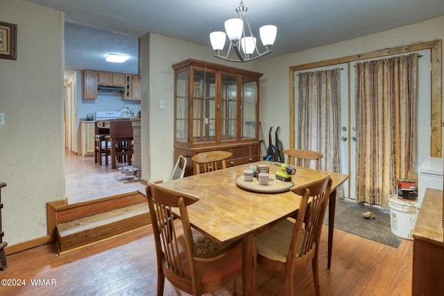 dining area featuring baseboards, a textured wall, light wood-type flooring, and a notable chandelier