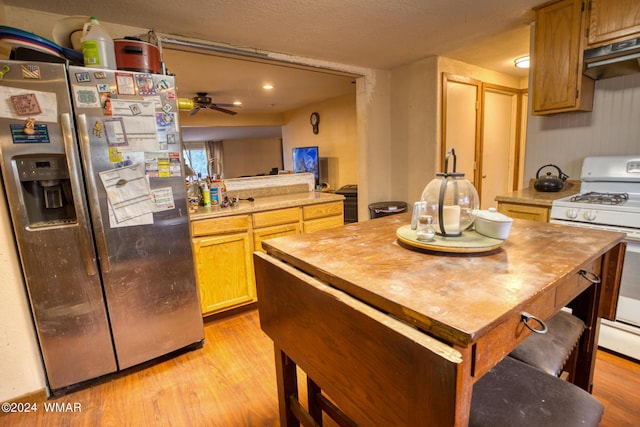 kitchen with white gas stove, extractor fan, light countertops, stainless steel fridge with ice dispenser, and light wood finished floors